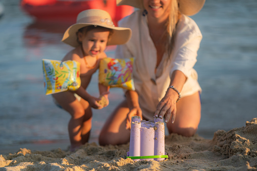 Close-up of mother and daughter building sand castle on the beach. Focus is on bucket
