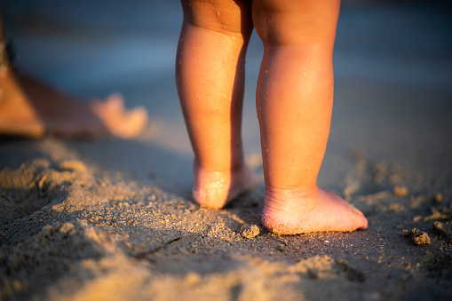 Close-up of cute unrecognizable toddler's legs on the sand at the beach