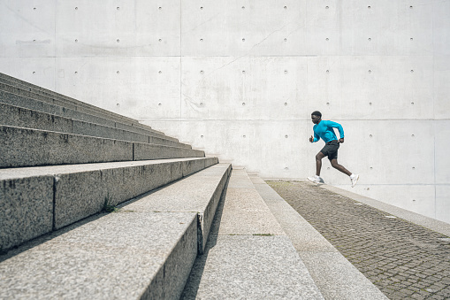 young sportsman running up steps in front of concrete wall outdoors in berlin at sunny day