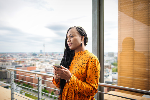 elegant black business woman with mobile phone standing on roof terrace with view on cityscape of Berlin