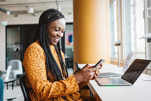 portrait of smiling black business woman looking at mobile in office