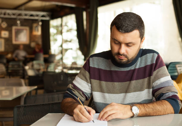 istock Handsome man is sitting at a desk and writing a letter. 1725767485
