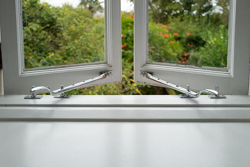 Shallow focus of chrome window handles seen on ajar windows located within a cottage bedroom. Seen looking out to the enclosed rear garden.