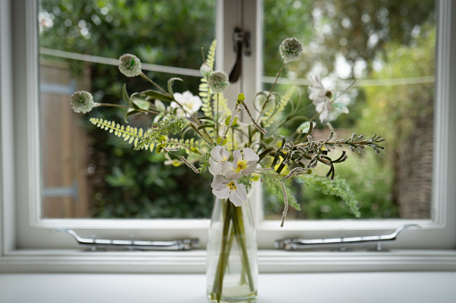 Shallow focus of artificial flowers seen on the ledge of a kitchen window looking out to a small, enclosed garden.