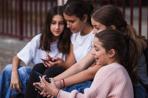 Girls sitting on a school staircase relaxed and using mobile phones, close-up