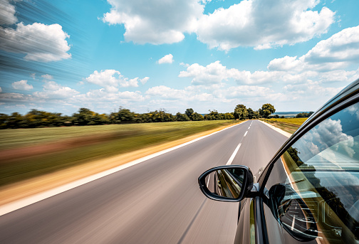 In the summertime, under the sunny sky, a car drives along the highway, creating a mesmerizing motion blur effect. As it speeds ahead, the surrounding environment becomes a blur of colors and shapes. Trees pass by in a rural landscape, accentuating the sense of a long journey. This exhilarating travel experience captures the thrill of speed and the allure of the open road.