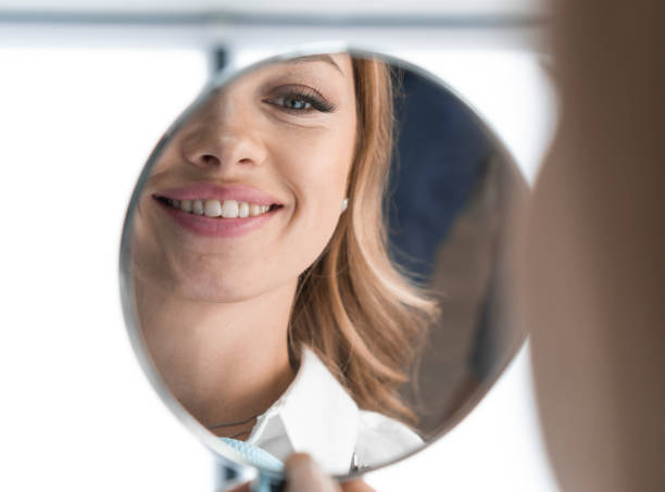 istock In mirror can see distinct improvements in condition teeth after visiting dentist. Woman is glad that can smile without complexes because her wonderful smile. After teeth whitening, implant placement 1725849553