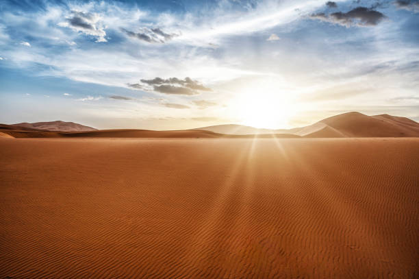 Desert dunes landscape with sun flare on cloudy sky background, Sahara, Morocco
