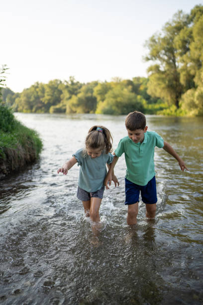 Young boy and girl playing together in the shallow part of river in nature.