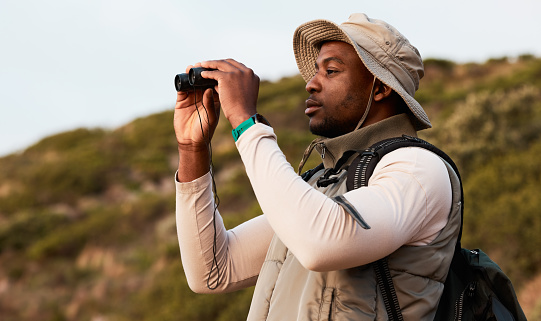 Hiking, binocular or black man on mountain in nature on trekking journey or adventure for freedom. View, holiday vacation or African hiker walking to search in park for exercise, fitness or wellness