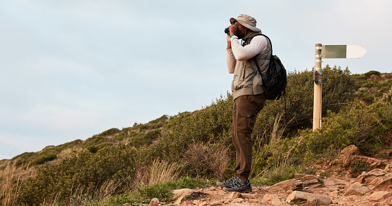 Hiker, binocular or black man on mountain in nature on trekking journey or adventure for fitness. Hiking, holiday vacation or African person walking to search in park for exercise or view on hill