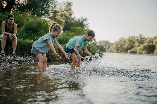 Young boy and girl playing together in the shallow part of river in nature.