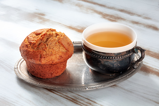 Orange muffin with tea on a rustic wooden kitchen table, on a vintage tray