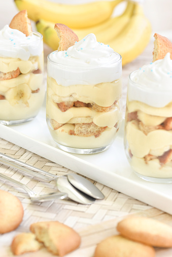 Homemade no-bake banana pudding in individual servings of a Southern USA classic dessert made with bananas, vanilla pudding, vanilla wafers and topped with meringue, with a bunch of bananas in background
