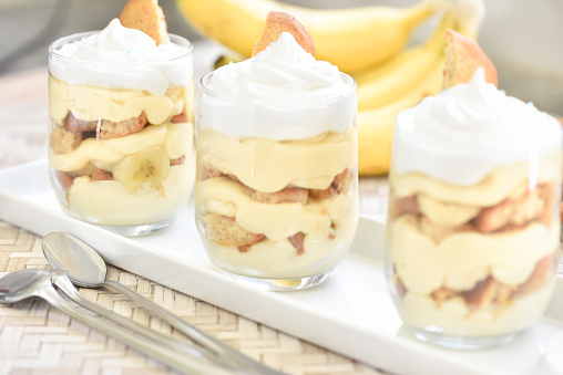 Homemade no-bake banana pudding in individual servings of a Southern USA classic dessert made with bananas, vanilla pudding, vanilla wafers and topped with meringue, with a bunch of bananas in background