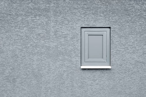 Small PVC window painted in gray on a gray textured wall. Room for copy space or text.