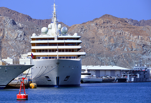 Wilayat Muttrah, Muscat, Oman: bow view of the Fulk al Salamah royal superyacht, one of the 8 vessels of the Oman Royal Yacht Squadron, the Sultan's fleet of pleasure craft, operated by the Diwan of Royal Court Affairs. Built at the T.Mariotti shipyard in Genoa, in 2016. At 164 metres (538 ft 1 in), Fulk Al Salamah is the second longest yacht in the world as of 2023. Mega yacht Moored at Port Sultan Qaboos (PSQ), Gulf of Oman / Arabian sea. Al Hajar Mountains in the background.