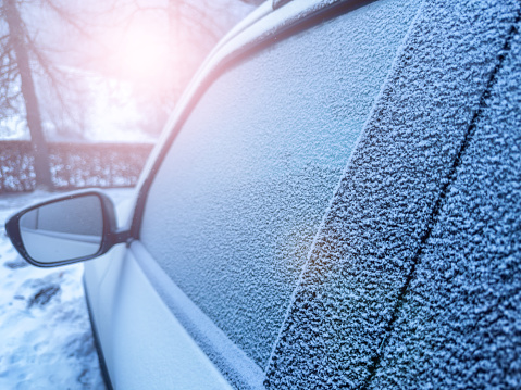 Window of the car covered with frost during winter morning and sun flare light reflecting