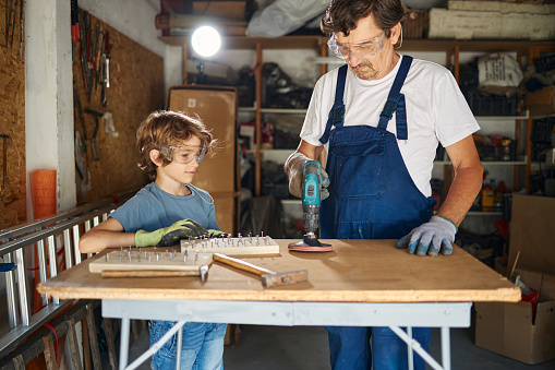 Grandfather and his grandson repairing old furniture in garage.