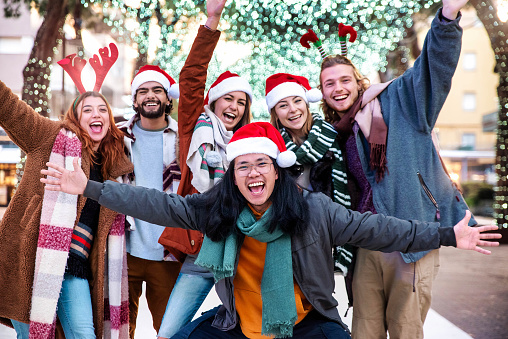 Happy friends wearing santa claus hat celebrating Christmas eve together - Young people having fun walking in Christmas market street - Winter holidays concept