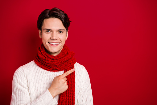 Portrait of handsome friendly boyfriend wear scarf direct finger empty space good news novelty information isolated on red color background.