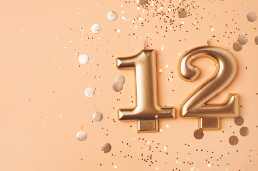 Gold candles in the form of number twelve on peach background with confetti. 12 years celebration.