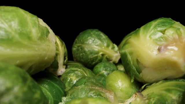 A camera moves through a multitude of Brussels sprouts on a black background. Dolly slider extreme close-up.