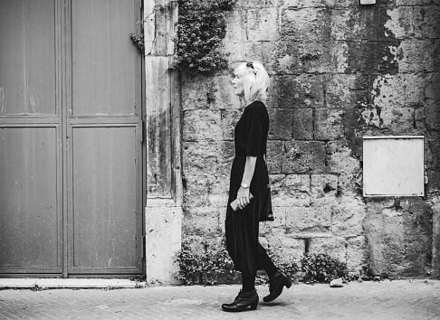 Monochrome image of a mature woman in a black dress walking along the alleys of the town of Siano, foothills east of Vesuvius and Naples, Italy. With some grain, but not much.