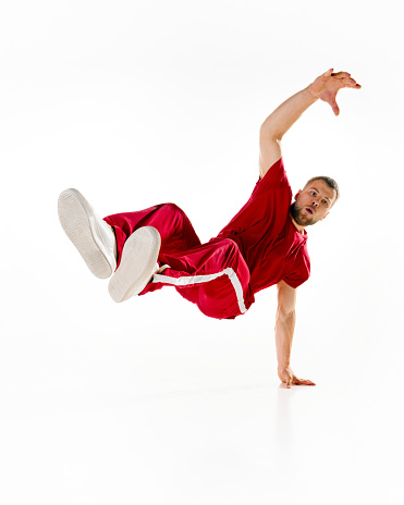 Air twist. Young sportive man, b-boy dancing hip-hop, breakdance on one hand raising legs up in motion against white background. Concept of youth culture, sport, action, active lifestyle. Copy space.