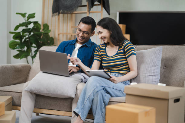 istock Young couple relaxing sitting on the sofa using the computer laptop around cardboard boxes, very happy moving to a new house. 1726081412