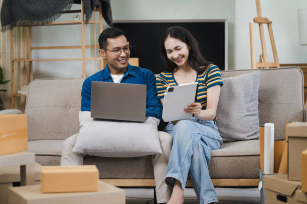 istock Young couple relaxing sitting on the sofa using the computer laptop around cardboard boxes, very happy moving to a new house. 1726081420