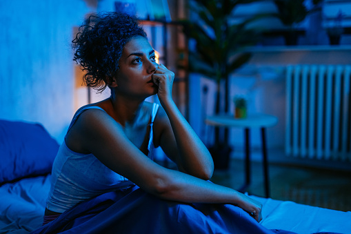 Young woman having insomnia while sitting on the bed at night in her bedroom.