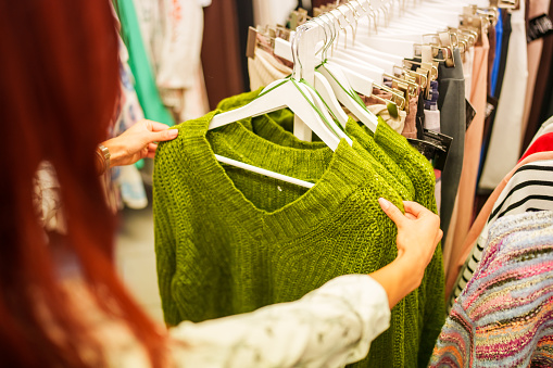 Warm sweaters. Autumn, winter clothes. Metal rack with various sweaters on hangers placed in modern fashion boutique