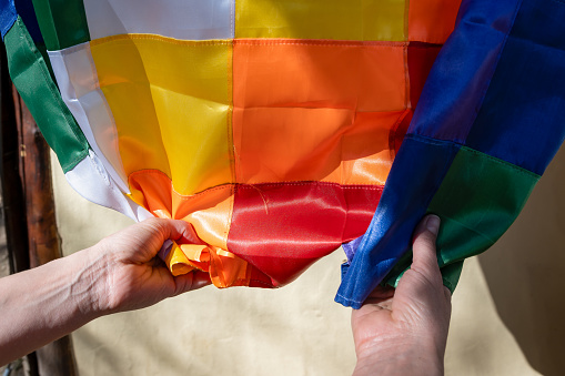 Close-up image of woman's hands clutching a silk Wiphala flag, a symbol commonly used to represent the native peoples of the Andes.