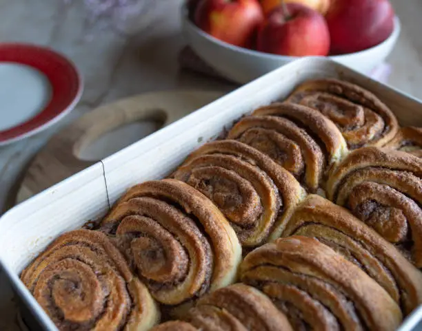 Homemade fresh baked danish cinnamon rolls. Caramelized with cinnamon sugar. Served warm and ready to eat in a baking pan on a table. Delicious autumn pastry.