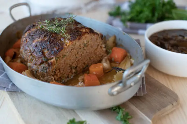 Delicious homemade german pork meatloaf with root vegetables in a roasting pan. Served with tasty brown onion sauce on a table.