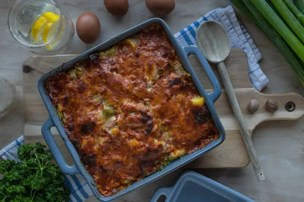 Delicious german autumn or winter food with a savory potato casserole. Cooked with cream, eggs, ham and leek. Topped with a tasta tomato cheese crust. Served hot and ready to eat on a table.
