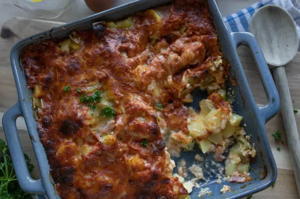 Delicious german autumn or winter food with a savory potato casserole. Cooked with cream, eggs, ham and leek. Topped with a tasta tomato cheese crust. Served hot and ready to eat on a table.