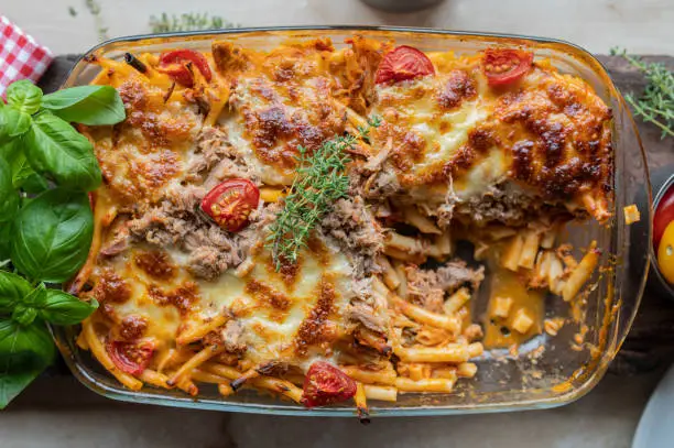 Delicious noodle casserole with macaroni, tuna, creamy tomato sauce and cheese crust. Served open and ready to eat on rustic background from above. Closeup