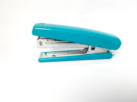 Simple pen type staple remover on the stapled blue and white sheets, new staples and small manual paper stapler on a white background