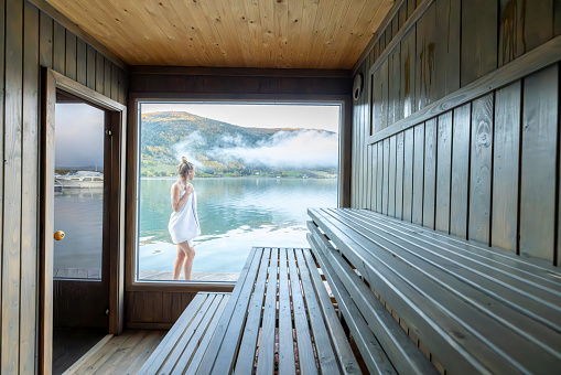Young woman relaxing outside a floating sauna, she refreshes and contemplates the nature