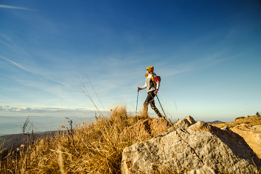 Side view of a female hiker with back pack and hiking poles on a mountain peak