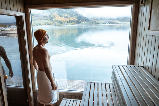Young man relaxing in a floating sauna, he looks at the view from the window