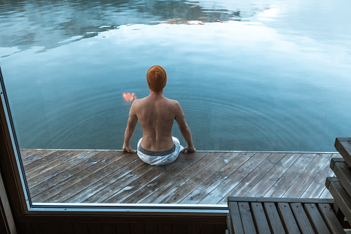 Young man relaxing in a floating sauna, beauty in nature. Lake view
