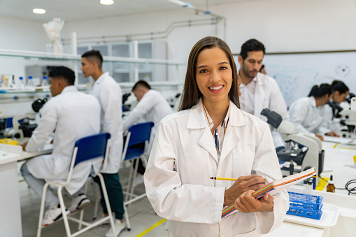 Portrait of a happy Latin American science student smiling at the lab while looking at the camera holding notebooks - STEM concepts
