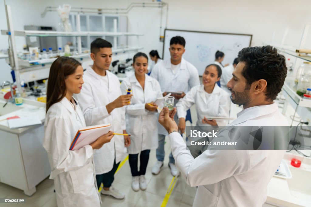 Science teacher showing a sample to a group of students at the lab Latin American science teacher showing a sample to a group of students at the lab - STEM concepts University Student Stock Photo