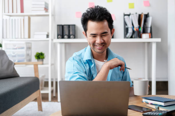 istock Young attractive man sitting on sofa at home working on laptop online, using internet, smiling, happy mood, freelancer, free leisure time, relaxed, modern job lifestyle 1726209373