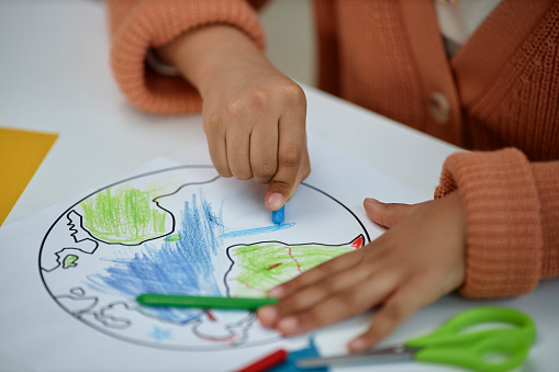 Close up of unrecognizable little girl coloring planet Earth in preschool, copy space