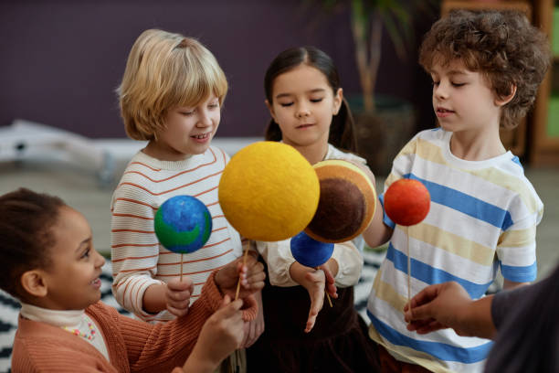 Diverse group of children holding planet models in preschool class and learning about space