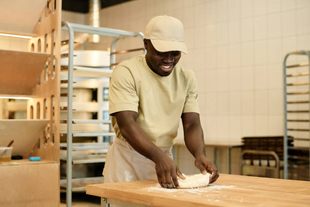 Smiling young man kneading dough working in artisan bakery